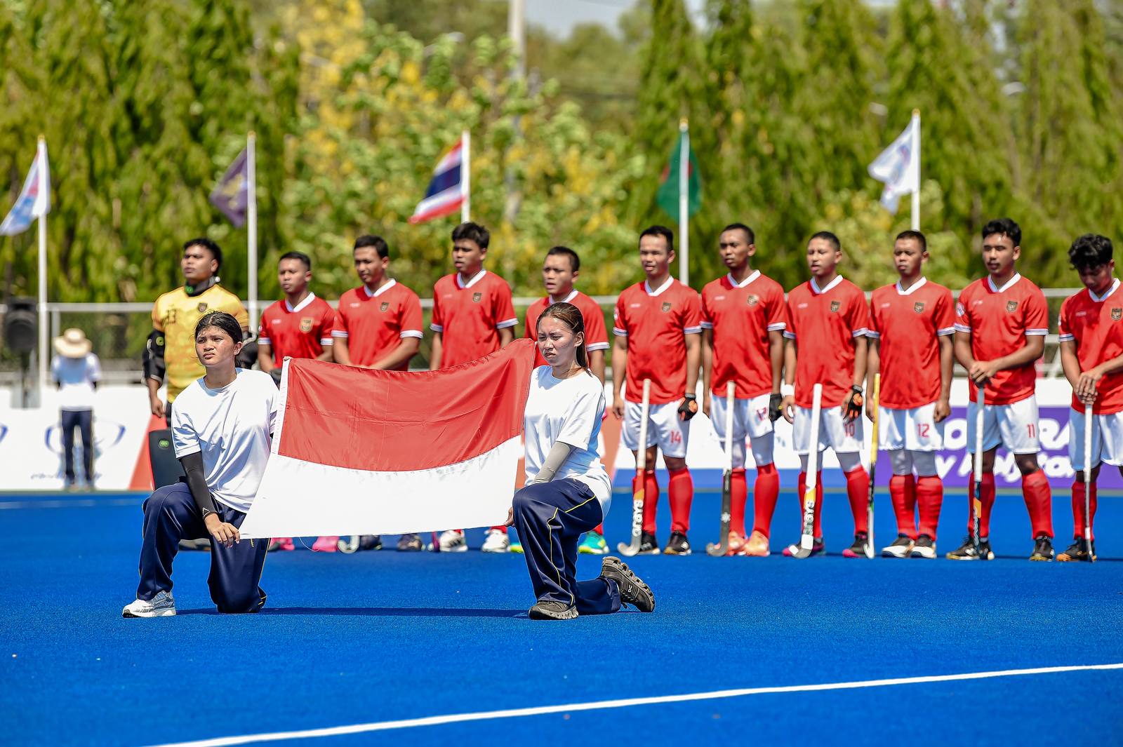Tim nasional hoki Indonesia berbaris membawa bendera Merah-Putih di lapangan.